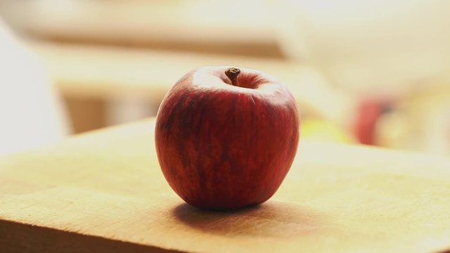 A dolly shot approaching a ripe red apple on a wooden chopping board with a soft blurred background.
