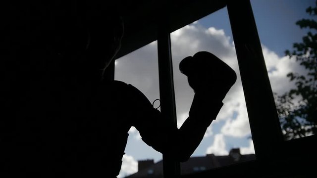 Silhouette of man is performing fighting exercises in fron of the window
