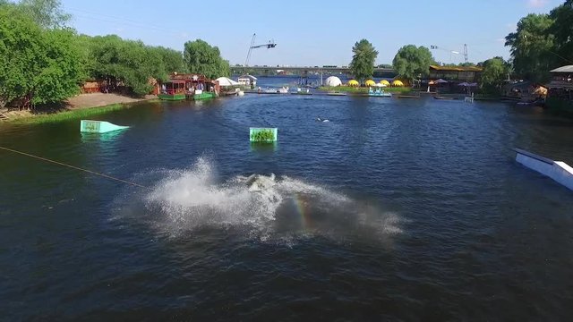 Flying over wakeboarding cable wake park HD aerial video. Wakeboarder doing jump tricks. Water extreme sport.