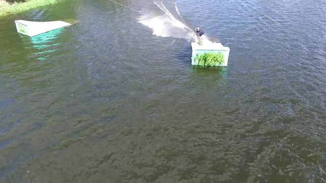 Flying over wakeboarding cable wake park HD aerial video. Wakeboarder doing jump tricks. Water extreme sport.