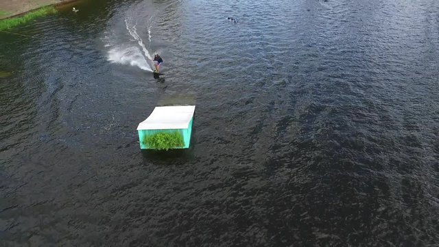 Flying over wakeboarding cable wake park HD aerial video. Wakeboarder doing jump tricks. Water extreme sport.