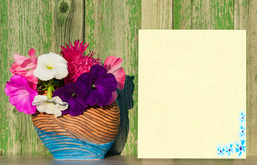 Mock up blank white sheet of paper on a wooden table with a vase and a bouquet of flowers against a green wooden wall vintage 
