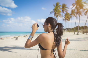 Cuban girl with smartphone dancing on the beach with palms, Cuba