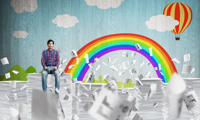 Young man sitting on pile of paper documents.