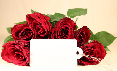 A bouquet of dark red roses with a white blank label on a wooden background