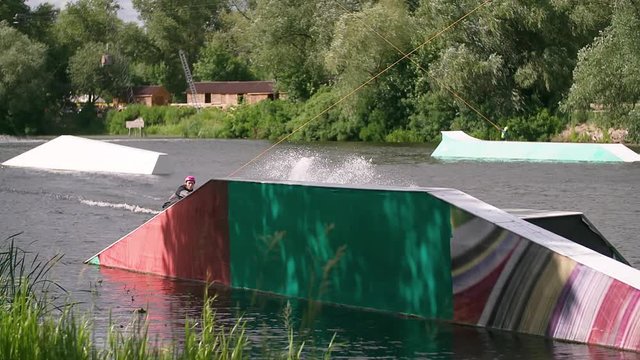 Wakeboarder doing tricks at cable wake park HD wakeboarding slow-motion video. Water extreme sport. Man jumps and rotates