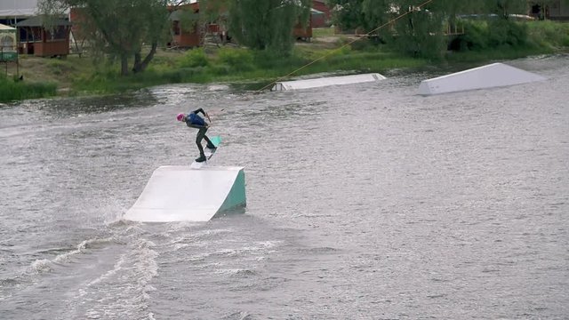Wakeboarder doing tricks at cable wake park HD wakeboarding slow-motion video. Water extreme sport. Man jumps and rotates on air