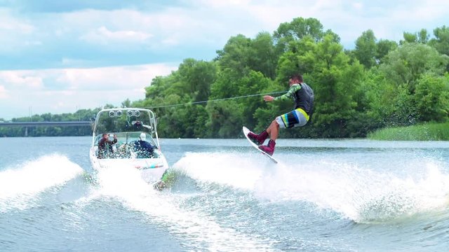 Wakeboarder doing tricks HD wakeboarding slow-motion video. Man rides behind boat and jumps somersault flip on waves. Water extreme sport.