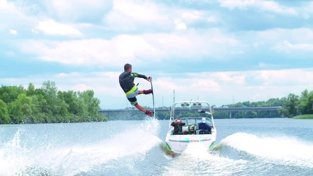 Wakeboarder doing tricks HD wakeboarding slow-motion video. Man rides behind boat and jumps somersault flip on waves. Water extreme sport.