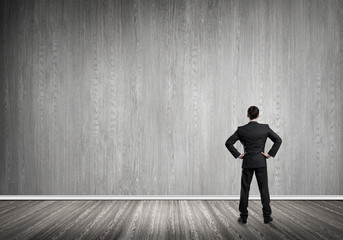 Businessman with hands on waist standing with back and looking at blank concrete wall