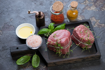 Black wooden serving tray with fresh seasoned medallion beef steaks ready to be cooked, studio shot
