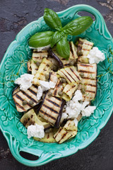 Top view of bbq slices of aubergines and zucchini with cheese, capers and olive oil served in a green dish, vertical shot