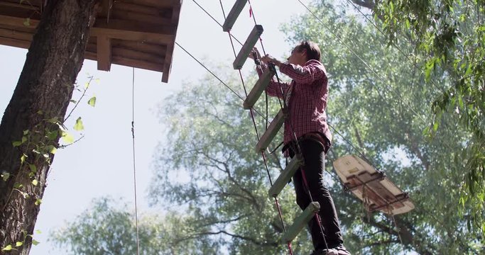 Male teenager climbs up on adventure rope park 4k video. Young climber moving on rope ladder for extreme adventure