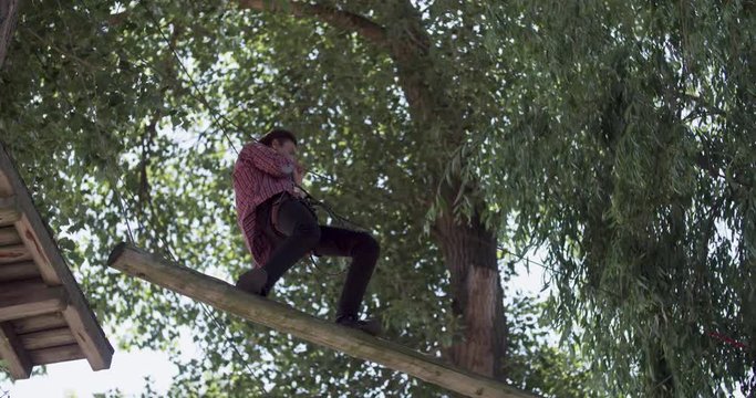 Male teenager moving on adventure rope park 4k video. Young climber walk on rope board for extreme adventure