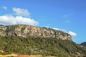 Naklejka premium Green Trees and Rock Cliffs Against Blue Cloudy Sky
