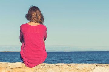 Fototapeta na wymiar Lonesome girl sitting on the coast and watching the sea / ocean.