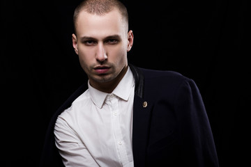 Stylish young unshaven man in a white shirt and black jacket  on a black background