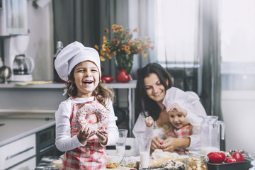 Small girl child eats a donut with my mom and sister happy cook at the table in the kitchen is lovely and beautiful