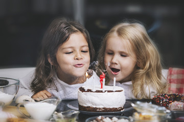 Two happy little girls child celebrating a birthday with cake at the table is lovely and beautiful