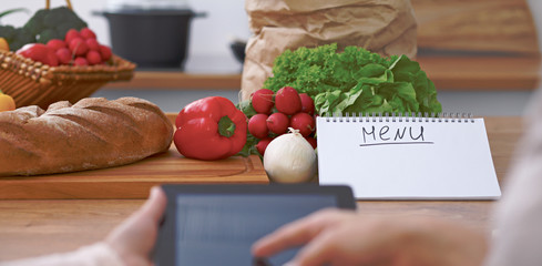 Close-up of four human hands are gesticulate over a tablet in the kitchen. Friends having fun while choosing menu or making online shopping. So much ideas for tasty cooking. 