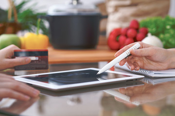 Close-up of four human hands are gesticulate over a tablet in the kitchen. Friends having fun while choosing menu or making online shopping. So much ideas for tasty cooking. 