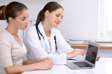 Fototapeta premium Doctor and patient sitting at the desk. Physician pointing into laptop computer. Medicine and health care concept
