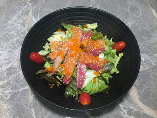 Sashimi salad in the black bowl on the marble table, Raw fish salad and tomato, Sprinkle with white sesame. 