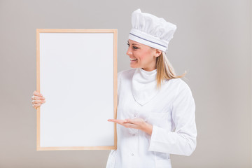 Portrait of beautiful female chef showing whiteboard on gray background.
