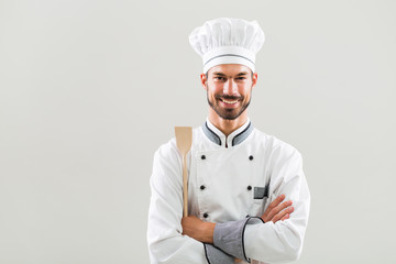 Portrait of smiling chef holding wooden spoon on gray background.