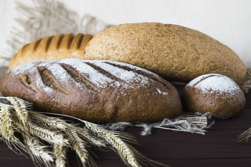 Rye, grain and white bread next to the spikelets of rye on a wooden table