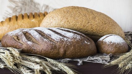 Rye, grain and white bread next to the spikelets of rye on a wooden table