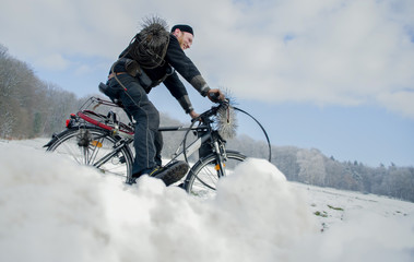 Schornsteinfeger mit Arbeitsgeräten fährt  Fahrrad in verschneiter Winter Landschaft 