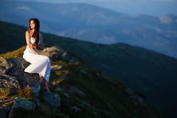 Beautiful young long hair woman posing in high mountain scenery. Pretty young woman sits on a rock