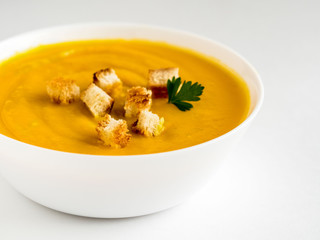 pumpkin soup with croutons and herbs in a white Cup on a white background