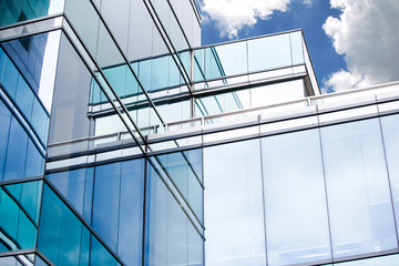 Obraz premium Blue sky and clouds reflecting in windows of modern office building