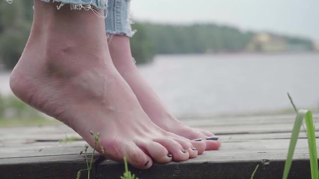 Close up of bare feet of girl standing on tips toes and trying to keep balance on wooden path
