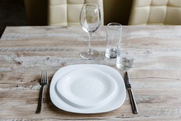 Table setting. Two white plates, one on top of another. Knife and fork. Wine glass, water glass and old fashioned glass. Wooden table. Selective focus.