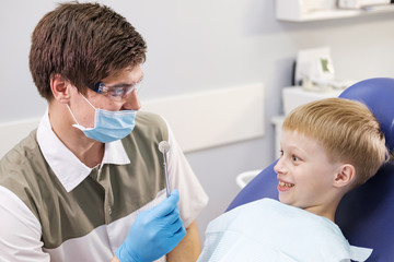 Obraz premium Male dentist examines the teeth of the patient cheerful boy.