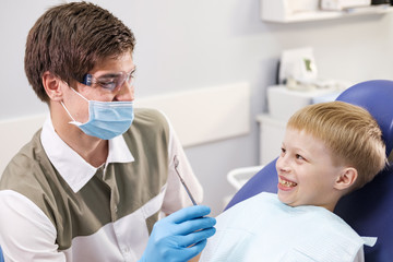 Obraz na płótnie Canvas Male dentist examines the teeth of the patient cheerful boy.
