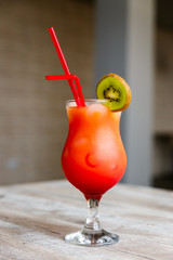 A colourful, bright red and orange cocktail in a high glass with a slice of green kiwi and two red straws. Selective focus.