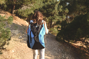 Woman hiker walks on the trail outside in forest with backpack and looking at the sea