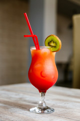 A colourful, bright red and orange cocktail in a high glass with a slice of green kiwi and two red straws. Selective focus.