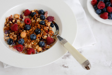 Healthy breakfast in a bowl with homemade baked granola, fresh berries and yogurt on a marble table.