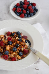 Healthy breakfast in a bowl with homemade baked granola, fresh berries and yogurt on a marble table.