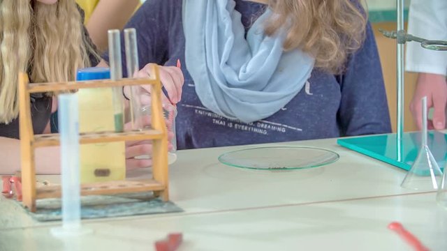 Two girls are focused on doing an experiment right in the chemistry class. They are trying to put something into a plastic cup.