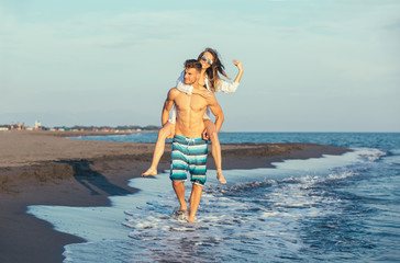 Happy couple in love on beach summer vacations. Joyful girl piggybacking on young boyfriend having fun.