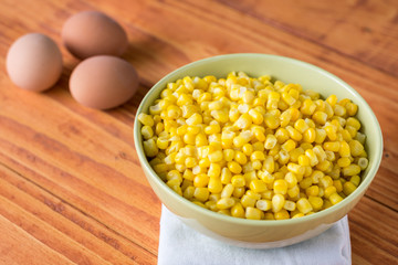Cooked corn in the bowl on the table with boiled eggs in the background