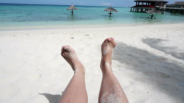 Relaxed feet playing with white sand at tropical island. POV sitting at beach seat