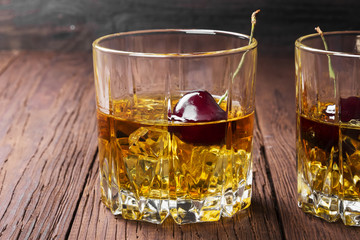 Cocktail from whisky with cherry in two glasses on a wooden background