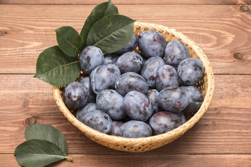 Fresh plum in a basket on a table with leaves and flowers